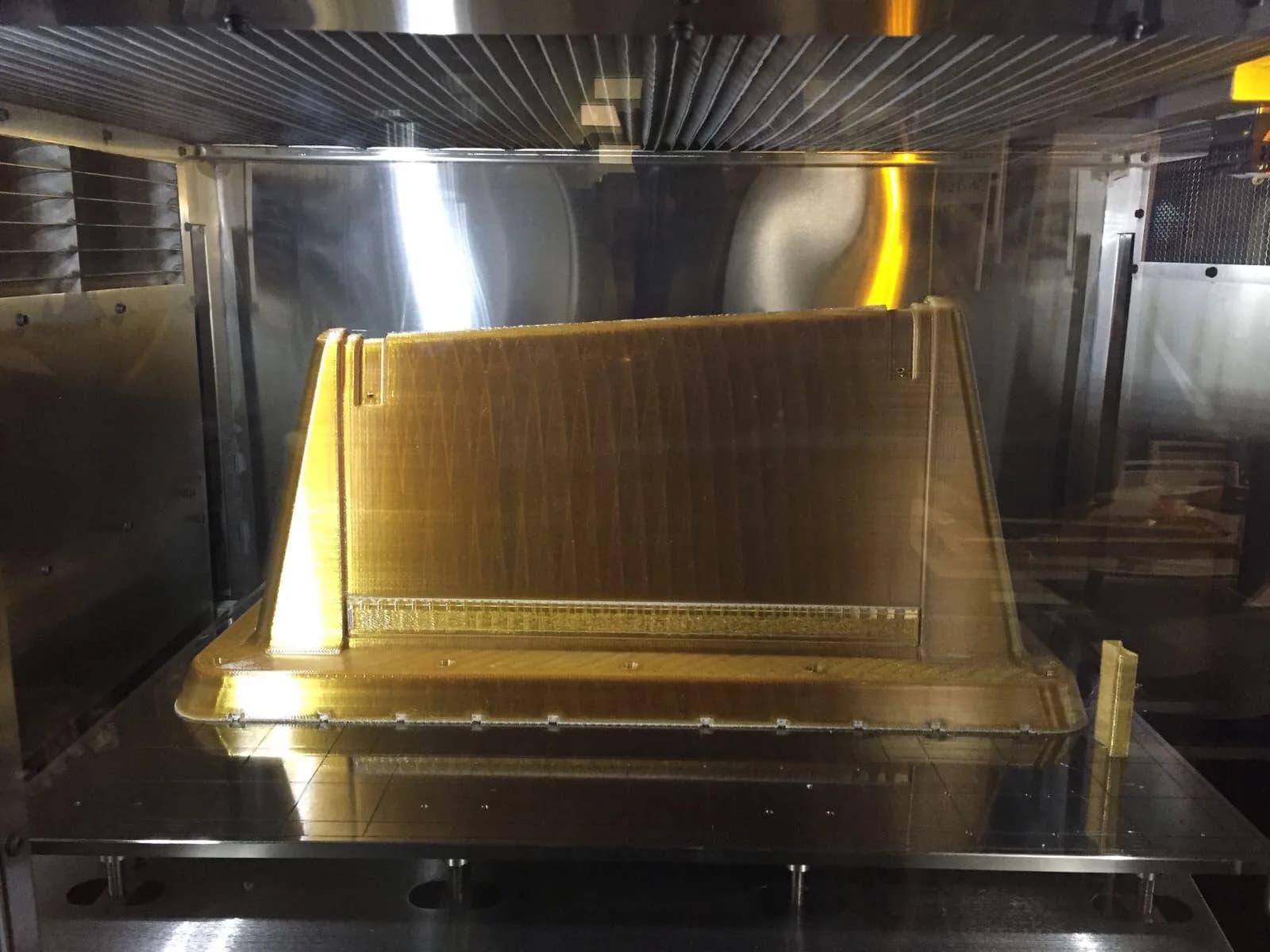 Large amber ULTEM 9085 panel part on the build sheet inside a Stratasys FDM chamber