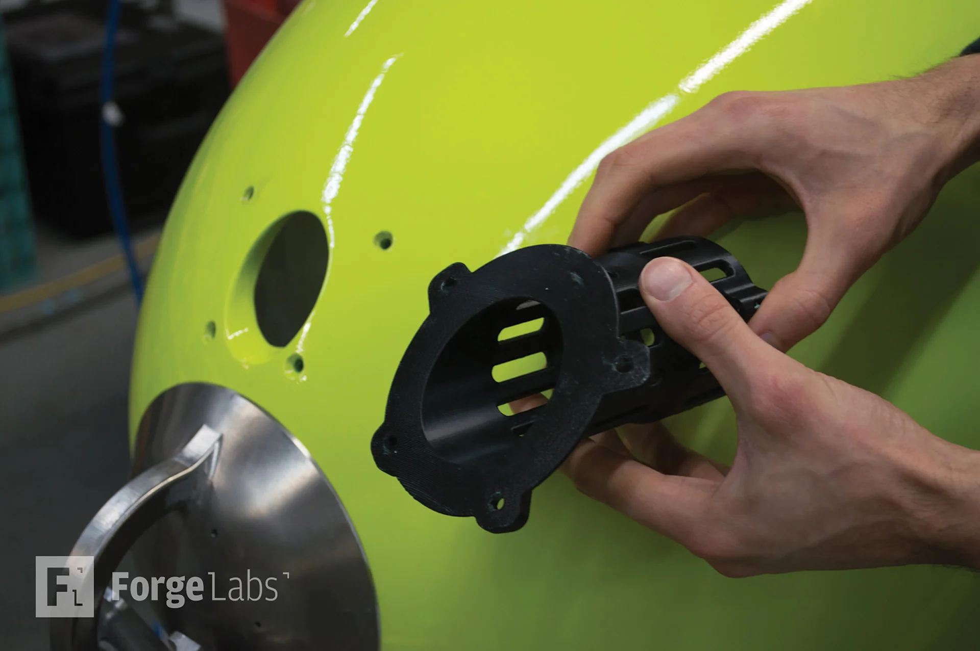Hand fitting a black 3D printed bracket into an opening in a green vehicle housing