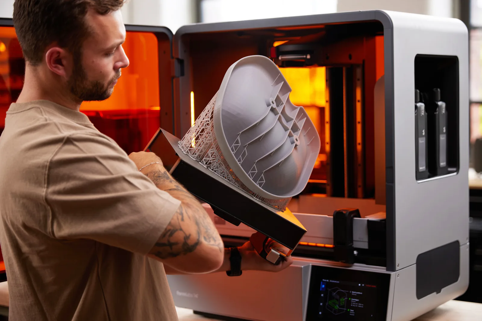 Operator lifting a build platform with a large grey SLA part on supports out of a Formlabs Form 4L printer