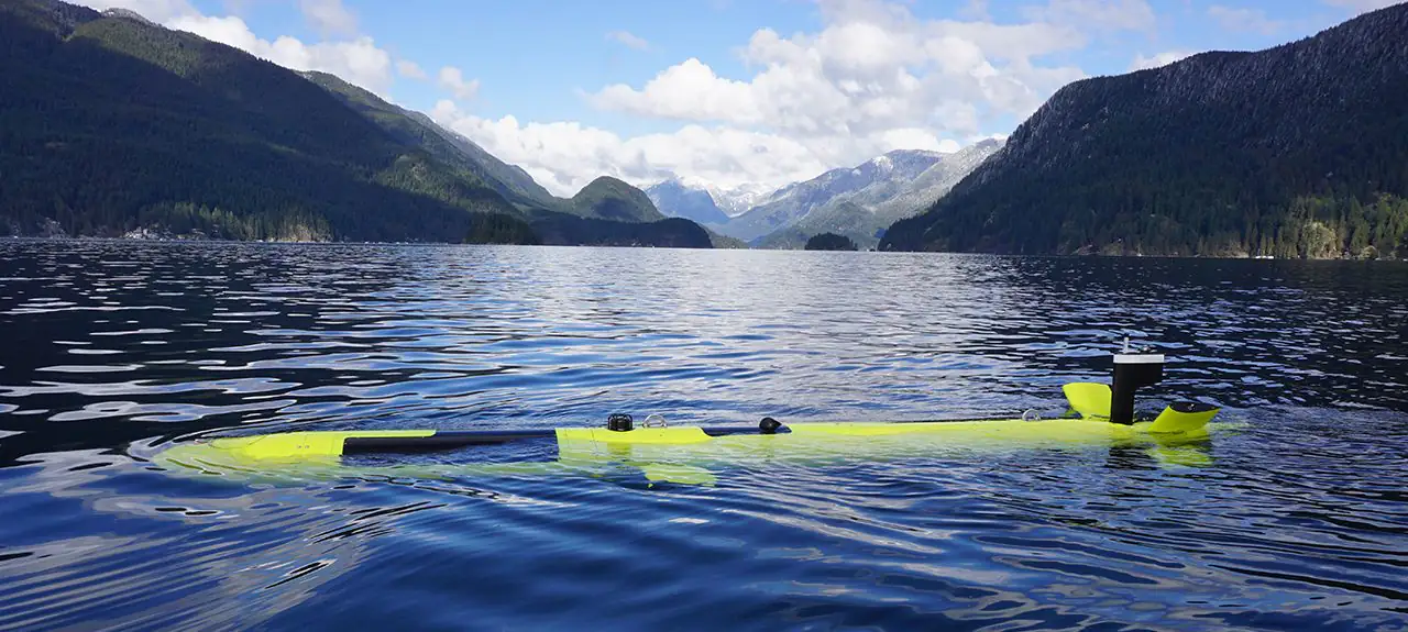 A yellow-green Explorer autonomous underwater vehicle floating awash on calm water